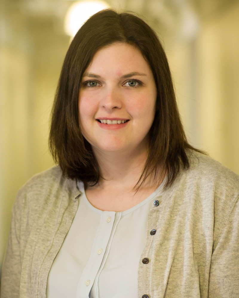 Professional portrait of a woman with shoulder-length brown hair wearing a light blouse and cardigan, photographed indoors with a softly blurred background.